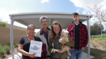 People pose for a photo. One person holds a small dog and another person holds a flier