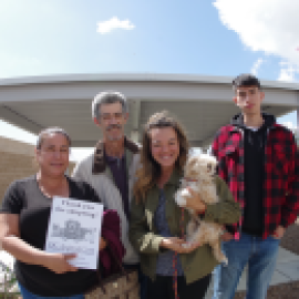 People pose for a photo. One person holds a small dog and another person holds a flier