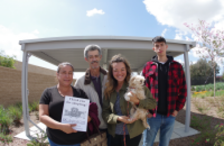 People pose for a photo. One person holds a small dog and another person holds a flier